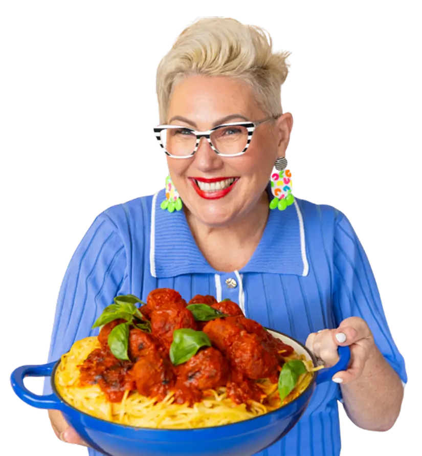 Steph de Sousa smiling and holding a pan of spaghetti topped with meatballs and basil, cut out on a transparent background.